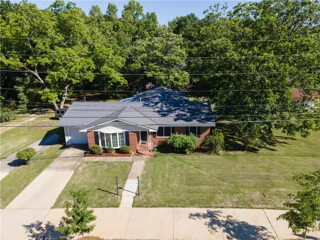 A classic brick residence features a durable metal roof and mature trees on a generous lot.