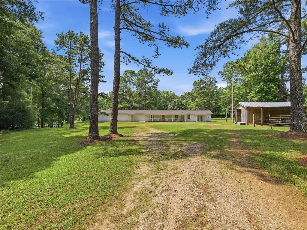 A long gravel driveway leads to a secluded ranch-style home surrounded by a generous lawn and mature trees.