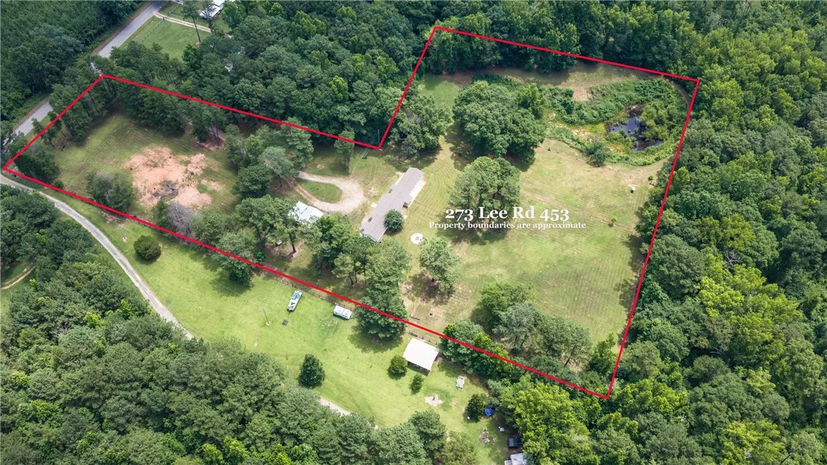 An aerial perspective reveals a secluded estate featuring verdant expanses, a winding driveway, and a tranquil pond.