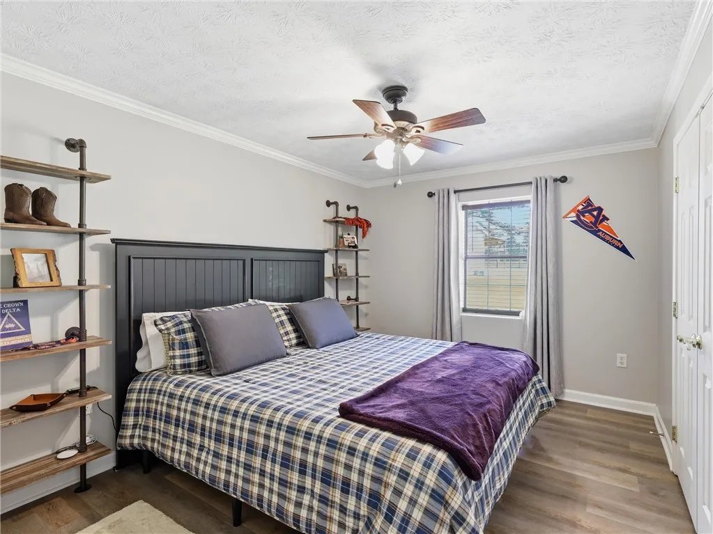 Relax in this comfortable bedroom featuring a ceiling fan, crown molding, and durable hardwood flooring.