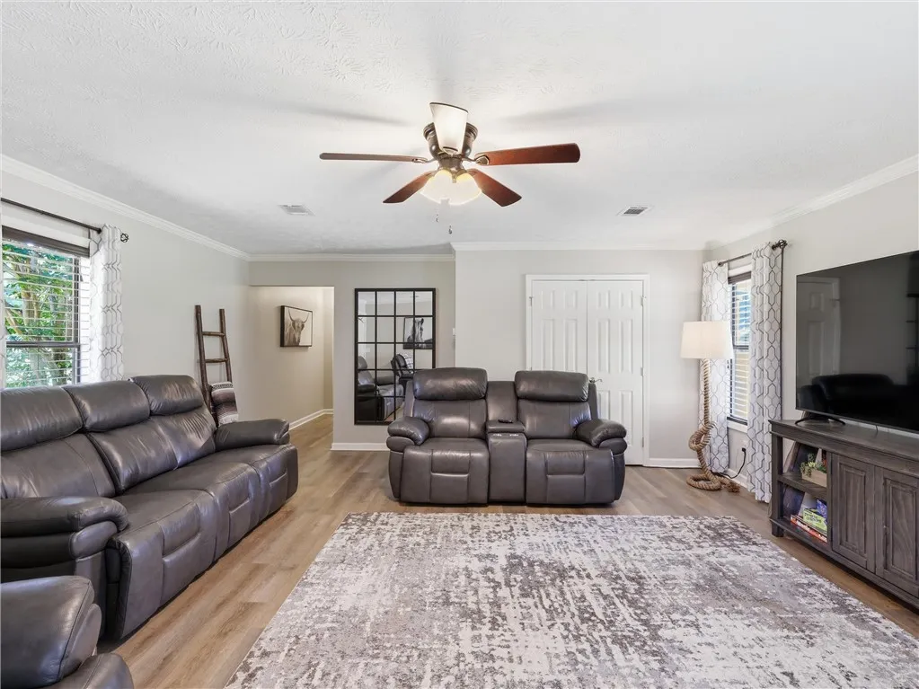 A well-lit gathering space featuring durable plank flooring and an overhead fan for comfort.