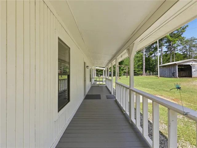 A deep covered porch provides a serene outdoor living space, overlooking a lush, verdant landscape.