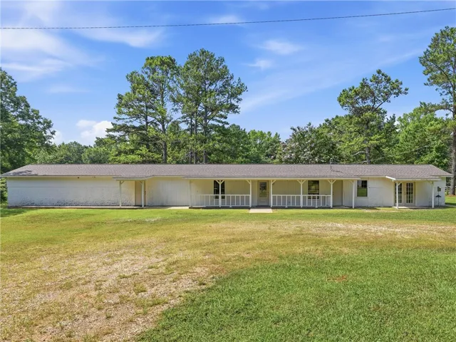 A spacious front porch adorns this residence, set against a backdrop of mature trees and a vibrant green lawn.