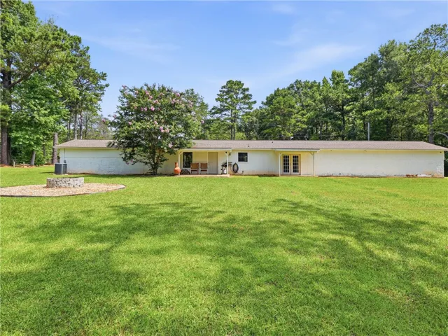 A spacious lawn provides ample outdoor living space with a fire pit and patio, all surrounded by mature trees.