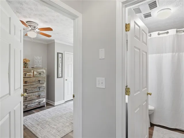 A well-lit bedroom features hardwood flooring and a stylish ceiling fan, with a full bathroom beyond.