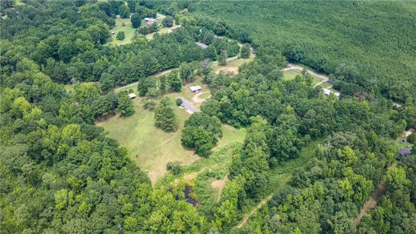 An aerial panorama reveals verdant woodlands surrounding a potential build site with a private pond.