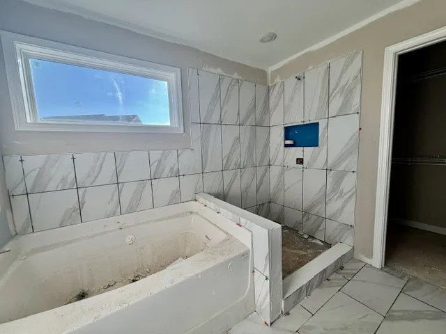 A window-lit primary bathroom featuring a spacious soaking tub and a walk-in shower with elegant tile work.