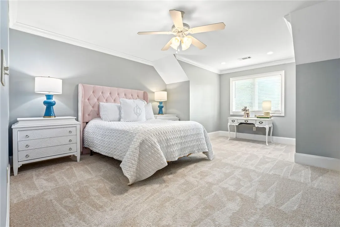 A well-lit bedroom features plush carpeting, crown molding, and a prominent ceiling fan for comfort.