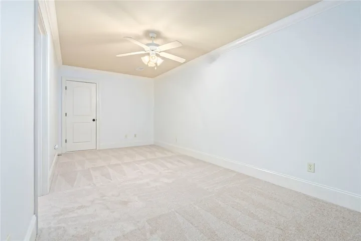 An inviting room features plush carpeting, crown molding, and a refreshing ceiling fan.
