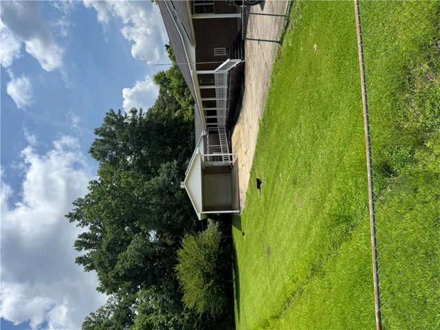 A well-maintained lawn stretches beside a house with an inviting, covered porch and mature trees.