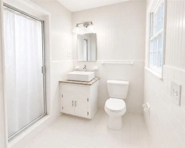 A well-lit primary bathroom features a shower, a vanity with granite counters, and classic white tile flooring.