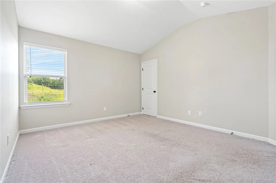An inviting room offering soft carpeting, a high vaulted ceiling, and ample light from the window.