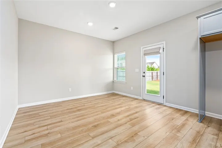 A well-lit room with wood flooring opens to a private yard through a glass-paneled door.