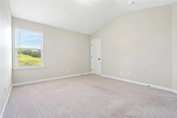 An inviting room offering soft carpeting, a high vaulted ceiling, and ample light from the window.