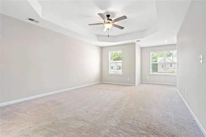 A spacious primary bedroom features a tray ceiling and plush carpeting, with ample light from multiple windows.