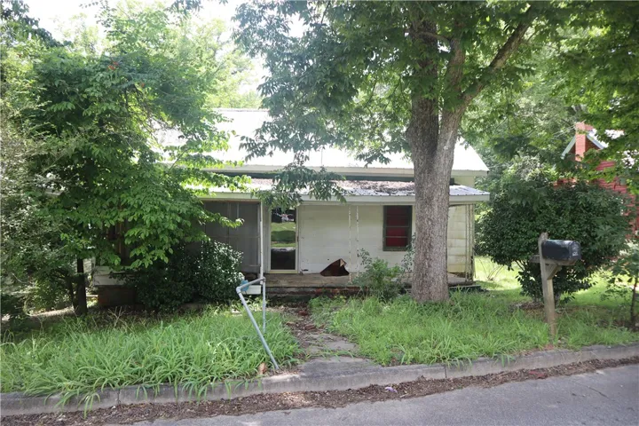 A modest home with mature trees and overgrown landscaping offers a serene retreat.