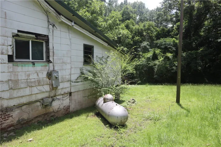A well-treed lot featuring a side view of a residence and a sizable propane tank.