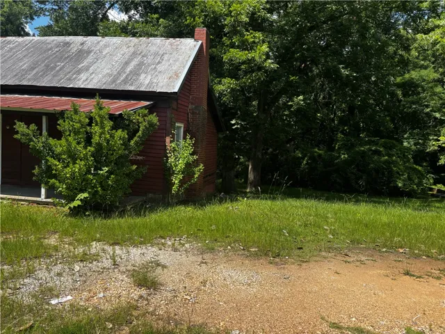 A classic red-sided structure with a metal roof and a brick chimney, nestled beside a verdant, mature tree line.
