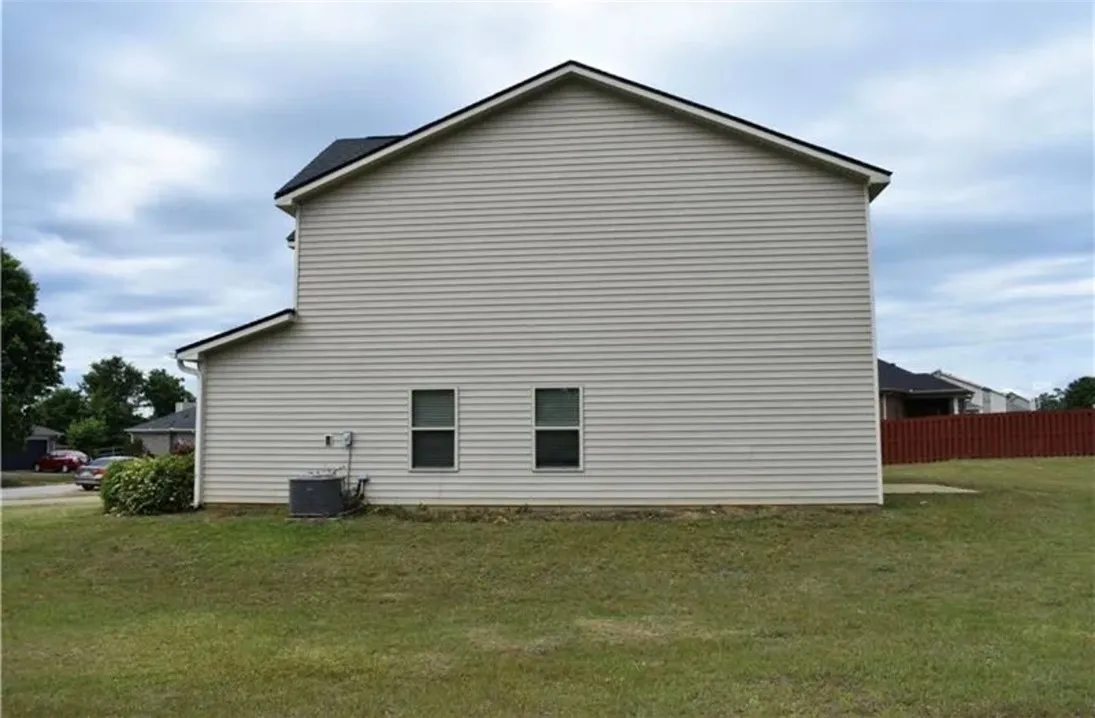 A well-maintained side profile of a two-story home, featuring classic siding and a lush, verdant lawn.