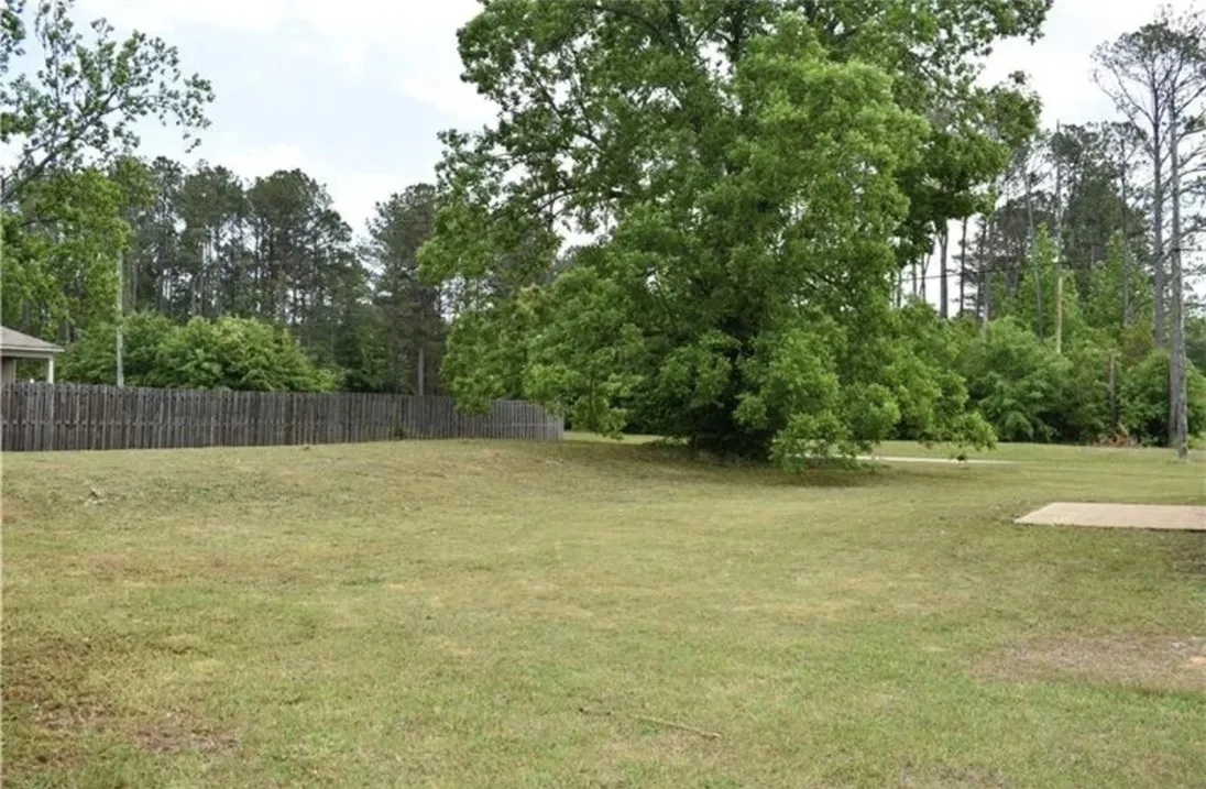 A spacious, verdant lot bordered by a classic wooden privacy fence, perfect for outdoor living.
