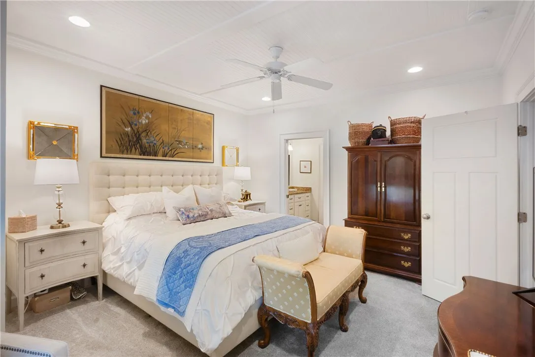 Recessed lighting and a classic ceiling fan illuminate this comfortable bedroom space, featuring a glimpse into the primary bathroom.