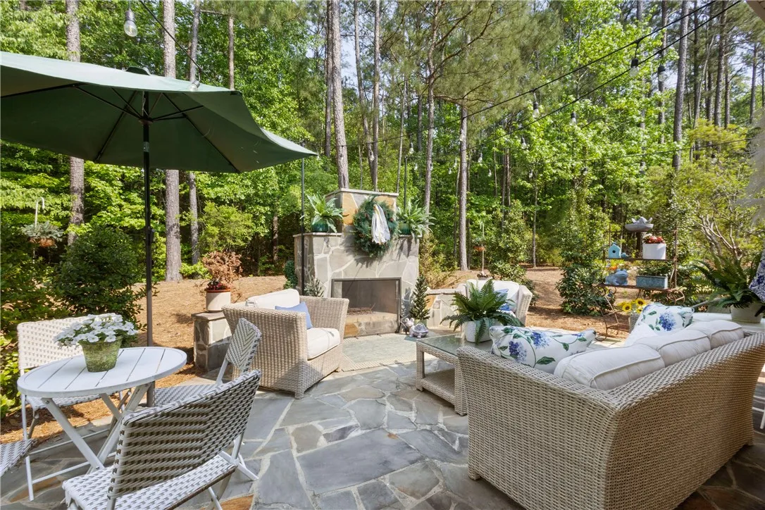 An inviting stone patio offers a private outdoor sanctuary, complete with a built-in fireplace and lush natural surroundings.