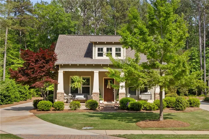 A charming cottage-style residence nestled among mature trees, featuring a welcoming front porch and well-manicured landscaping.