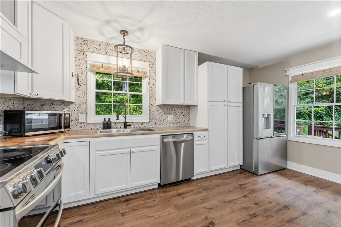 A well-equipped kitchen features durable flooring and bright cabinetry, overlooking a leafy outdoor space.