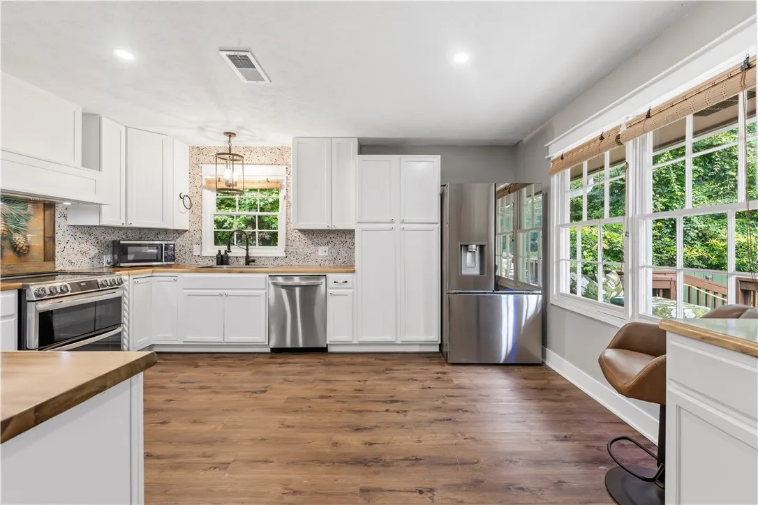 A contemporary kitchen features bright white cabinetry, wood countertops, and gleaming stainless steel appliances.