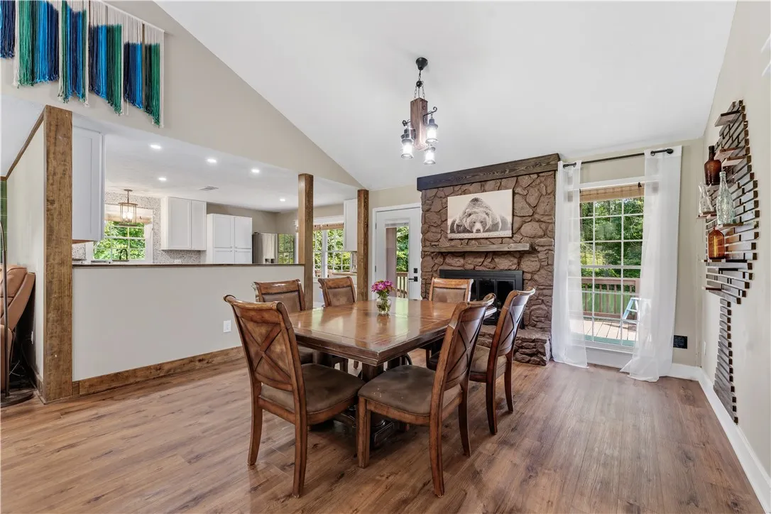 A stone fireplace anchors this open-concept dining area with vaulted ceilings and rich wood flooring.