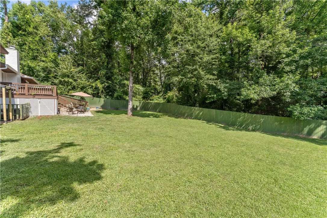A spacious backyard with mature trees, a wooden deck, and a fenced perimeter for peaceful outdoor enjoyment.