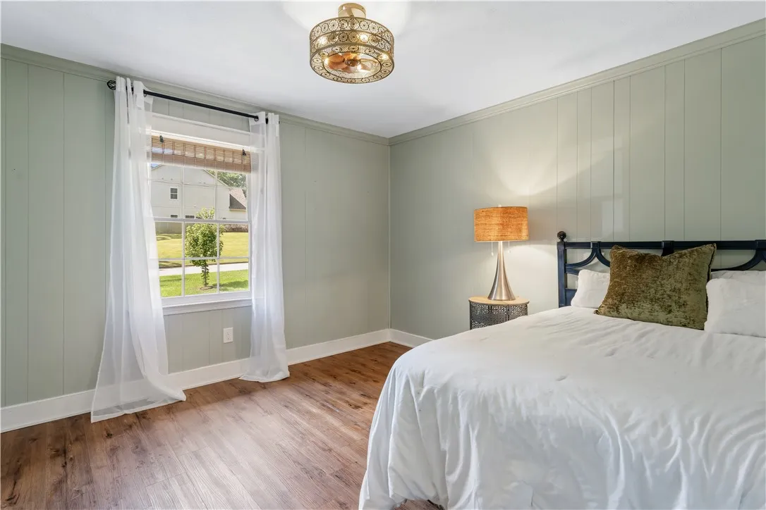 Laminate flooring and vertical wood paneling create a serene bedroom retreat with ample natural illumination.