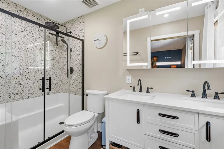A sleek modern bathroom features a spacious shower, a well-appointed vanity, and illuminated mirrors.
