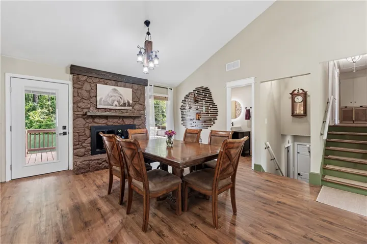 A striking stone fireplace anchors this dining room, offering direct access to an outdoor deck and featuring rich wood flooring.