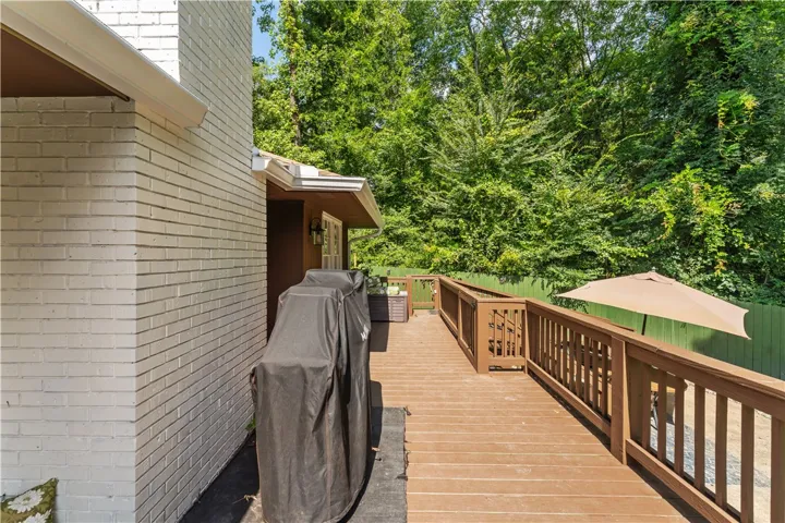 A spacious outdoor deck with wood railings offers a perfect setting for entertaining amidst lush greenery.