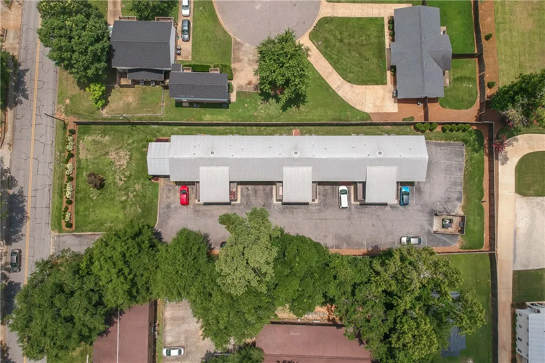 An aerial perspective reveals a long commercial building with individual bays and ample parking, bordered by a green lawn and mature trees.