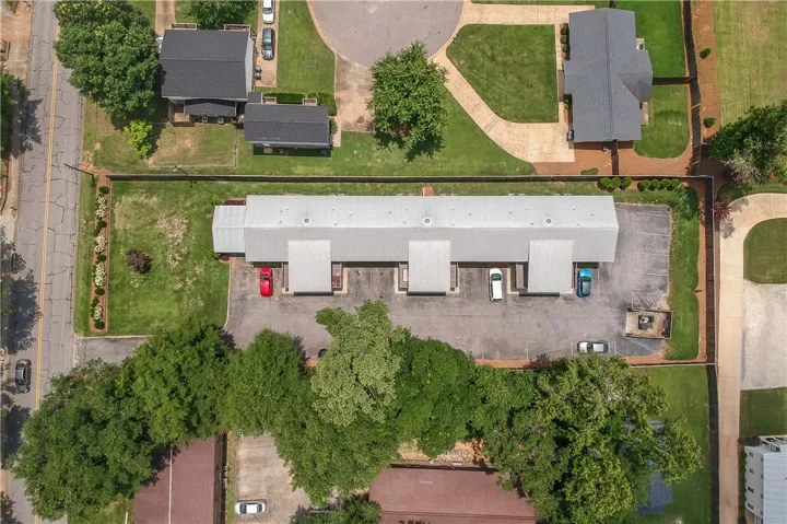An aerial perspective reveals a long commercial building with individual bays and ample parking, bordered by a green lawn and mature trees.