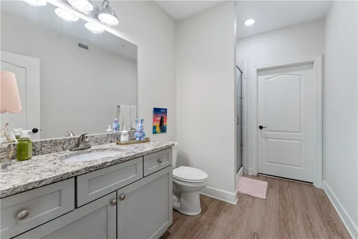 A well-appointed bathroom features a gray vanity with granite counters, a spacious mirror, and wood flooring.