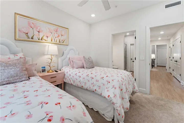 A well-lit bedroom offers two beds, plush carpeting, and direct access to a nearby bathroom.
