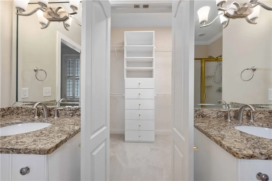 Double vanities with stone counters frame a dedicated walk-in closet for effortless organization.