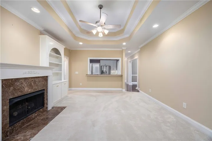 A refined living area boasts a tray ceiling, recessed lighting, and a prominent fireplace with built-in shelving.