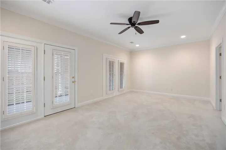 An airy bedroom offers plush carpeting, shuttered French doors, and soft recessed lighting.
