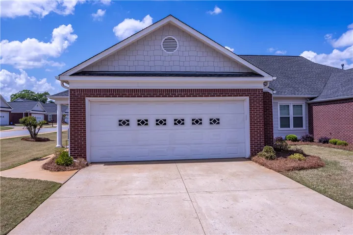 A well-maintained concrete driveway leads to a classic brick facade with an attached garage.