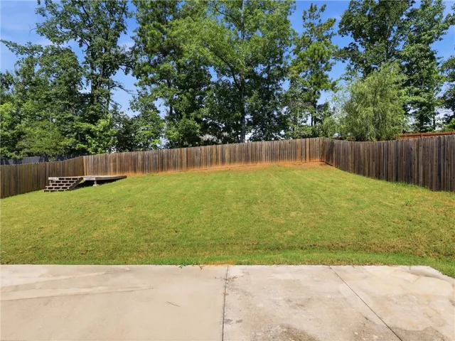 A spacious, sloped lawn offers ample outdoor enjoyment, bordered by a privacy fence and mature trees.