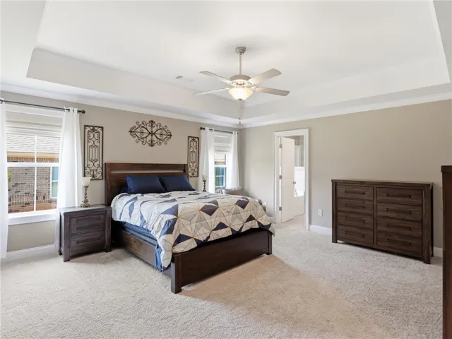 Relax in a generously proportioned bedroom featuring a tray ceiling and soft carpeting.