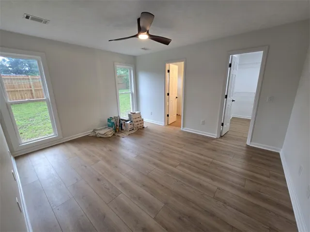 A well-lit bedroom with modern wood-style flooring and a functional ceiling fan.