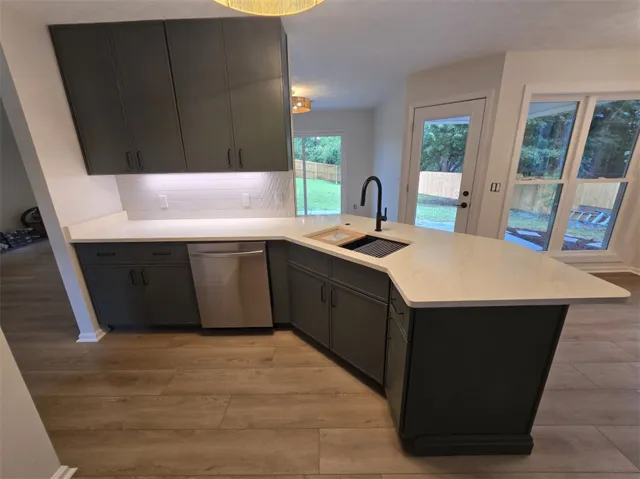 Modern kitchen features a sleek island with a black faucet, complemented by light wood flooring and backyard views.