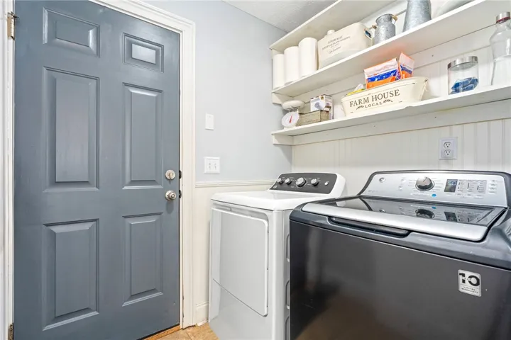 Functional utility space boasts modern washer and dryer units, complemented by practical wall shelving for organization.
