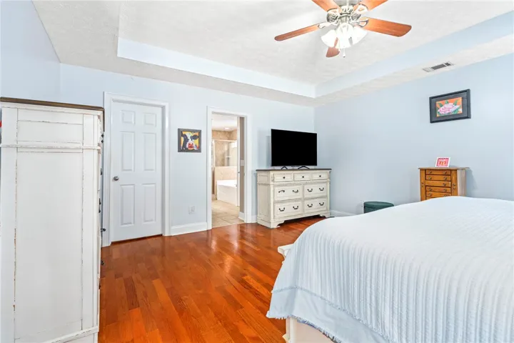 Hardwood floors complement the spacious bedroom with a tray ceiling and a ceiling fan.