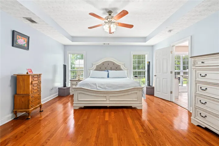 Rich hardwood flooring complements the tray ceiling and ceiling fan in this spacious bedroom.